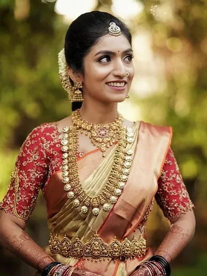 A bride in a gold and red Kanchipuram saree. Her custom red blouse is fully embroidered with intricate gold threadwork, creating a rich and regal bridal look.
