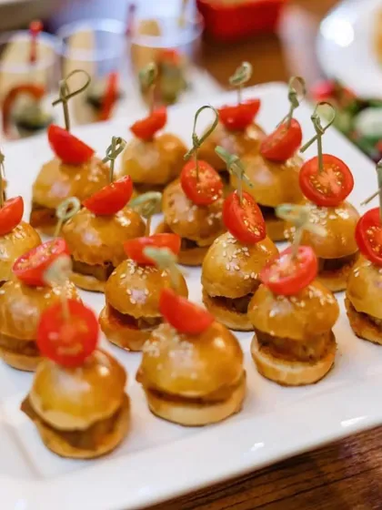Double the bites, double the flavor. This platter features adorable mini sliders topped with cherry tomatoes, a perfect bite-sized snack for any event.