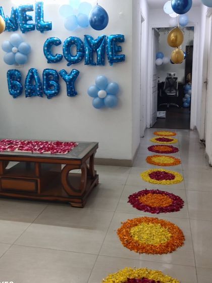 A 'Welcome Baby' decoration for a home entrance. This includes blue foil letter balloons and a pathway decorated with flower petal rangoli.