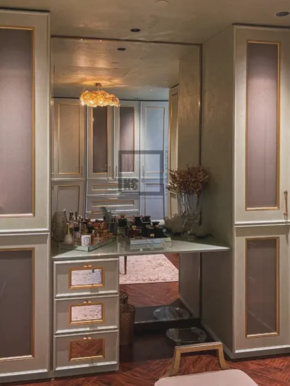 For a softer, more classic feel, this walk-in wardrobe uses gentle mint tones with elegant gold mouldings. The design includes a built-in vanity table with a large mirror, creating a bright and functional personal space.