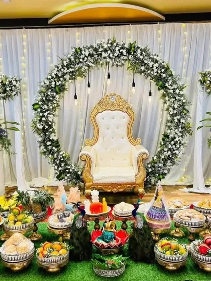 For a more modern and elegant look, I designed this Half Saree function stage with a beautiful white floral arch, hanging lights, and coordinated flower stands. The seer plates are arranged on a lush green mat, blending tradition with contemporary style.