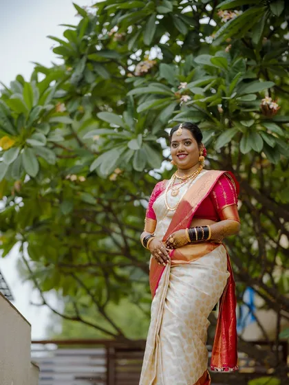 A portrait of a bride on her muhurtham day, dressed in a beautiful white and red saree, smiling warmly.