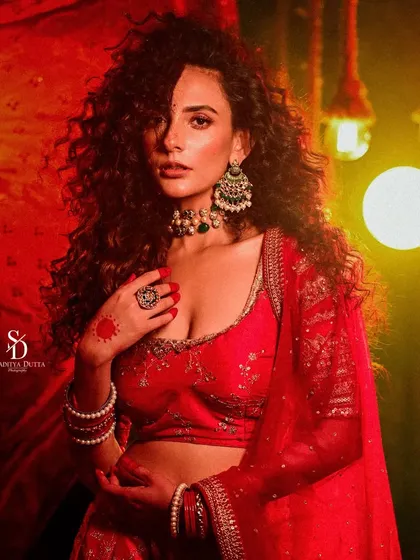 A dramatic, low-light portrait of a model in a red lehenga. The warm, glowing lights in the background create a festive and celebratory mood, perfect for a wedding or event look.