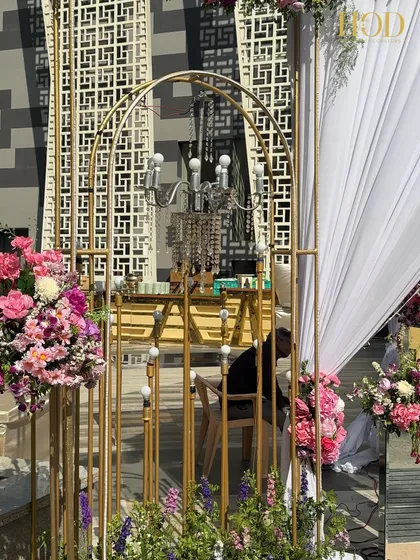 A detail shot of the entrance decor, featuring a golden cage-like structure with a mini chandelier inside, surrounded by beautiful pink and purple flowers.
