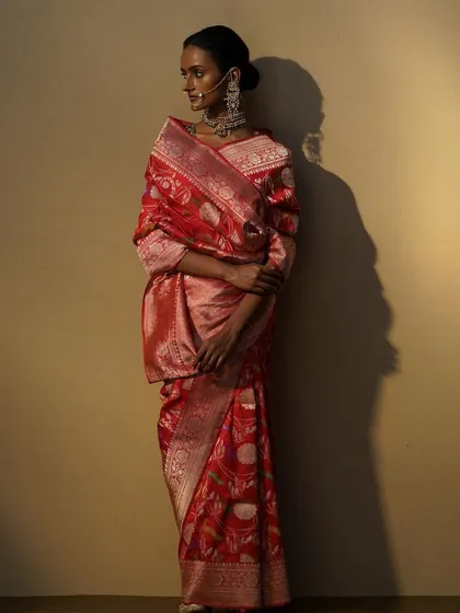 A stunning red Banarasi saree styled for a heritage campaign. The model's pose and the dramatic lighting are used to emphasize the rich texture and intricate weaving of this timeless piece.