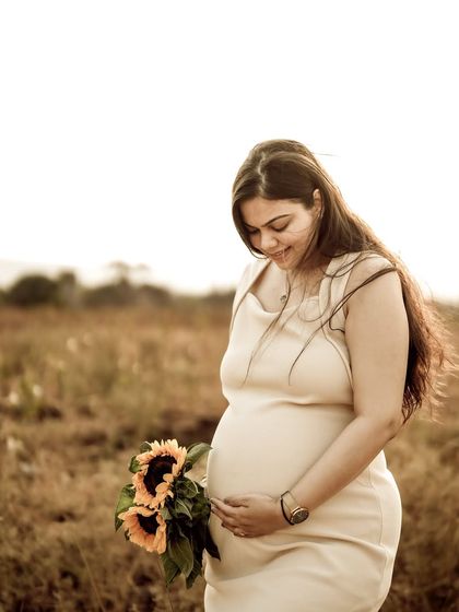 A serene portrait of the mom-to-be in a golden field, looking down at her bump with a gentle smile while holding sunflowers.
