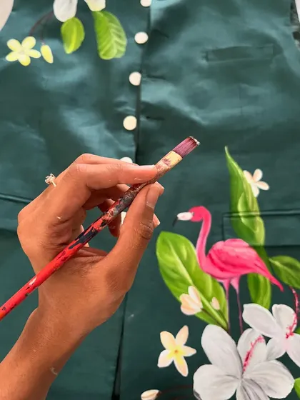A work-in-progress shot of a tropical-themed jacket. Here, I'm adding details to a bright pink flamingo nestled among lush green leaves and white flowers on a dark green fabric.