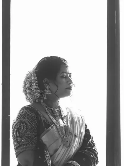 A high-key black and white portrait of a bride looking out a window. The bright white background creates a minimalist and ethereal feel, focusing on her silhouette.