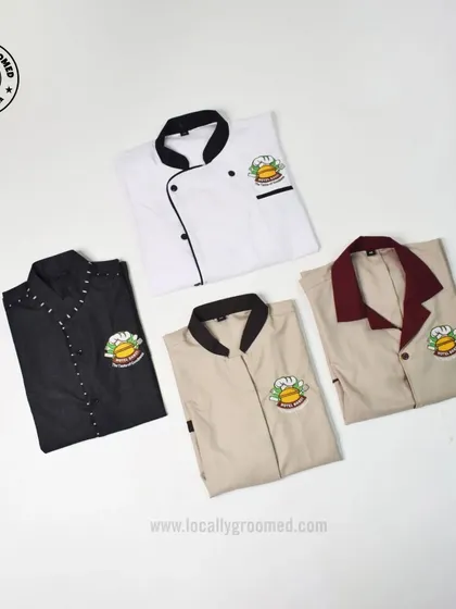 A display of custom uniforms designed for the hospitality industry. This collection includes a professional chef's coat and various staff shirts, all featuring an embroidered logo, showcasing our ability to provide a consistent and professional look for your entire team.