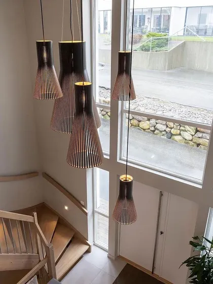 A cascading installation of Secto Design pendants in a modern staircase. The natural walnut veneer adds a rich, warm tone to the bright, airy space.