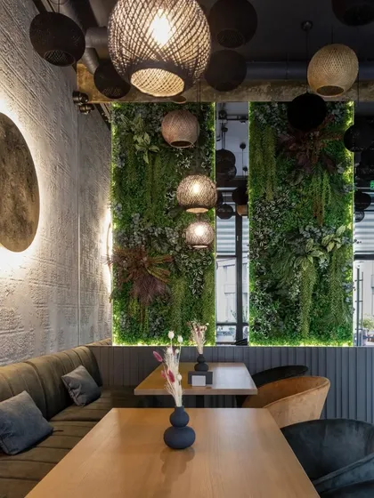 A dining nook with a plush, dark green sofa and vertical green walls. The spherical woven pendant lights add a natural, textural element to this moody and intimate corner.
