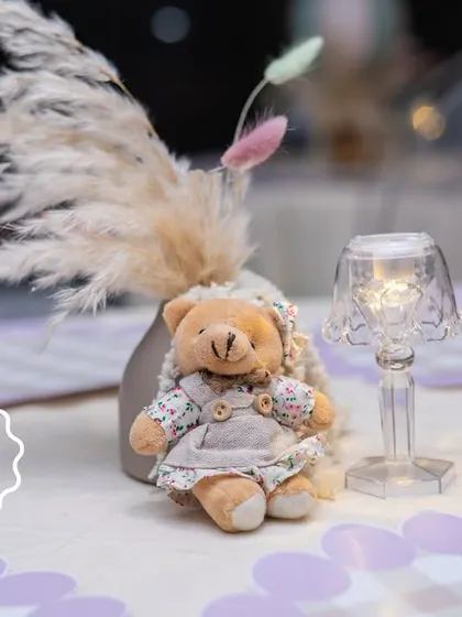 Another sweet table detail, featuring a teddy bear in overalls sitting next to a pampas grass arrangement and a miniature lamp.