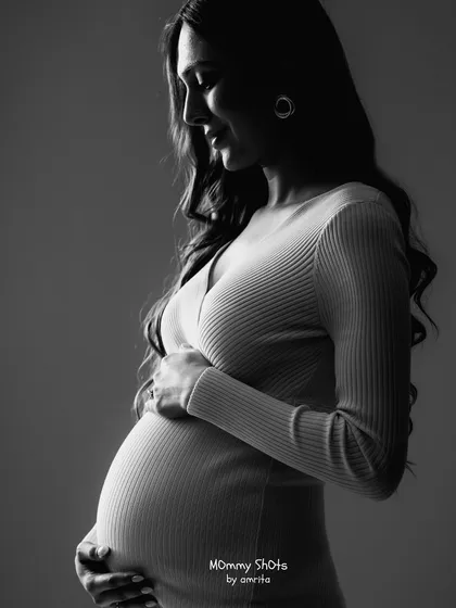 A classic low-key maternity portrait in black and white, focusing on form and shadow.