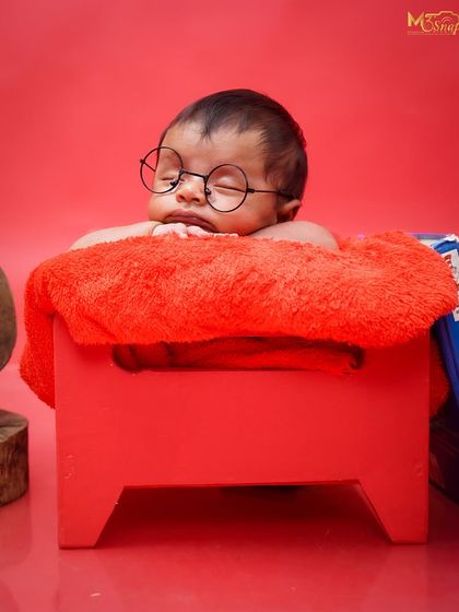 A tiny scholar deep in thought. This newborn with little round glasses on a bright red stool is a perfect example of a fun and creative themed shoot.