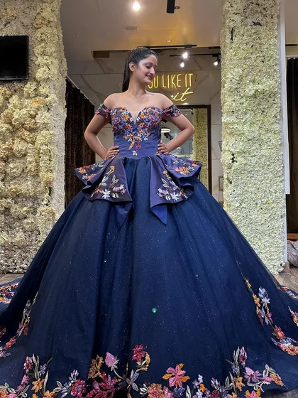 Our dreamy navy blue ball gown with colorful floral embroidery. This full-length shot shows the unique peplum detail at the waist and the magnificent trail, making it a standout choice for any formal event.