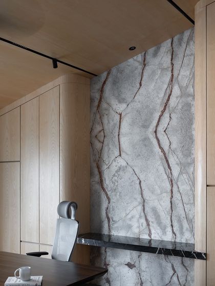 A home office featuring a stunning book-matched marble accent wall. The light oak paneling and minimalist desk create a space that is both luxurious and calming.