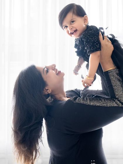 A joyful mother lifts her daughter in the air, both of them smiling brightly.