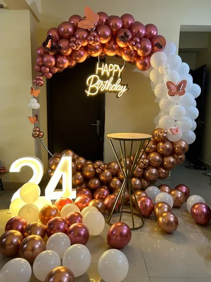 This elegant and modern ring backdrop is perfect for home celebrations. The setup features a circular frame with a rose gold and white chrome balloon arrangement, a 'Happy Birthday' neon sign, and a light-up marquee number '24'.