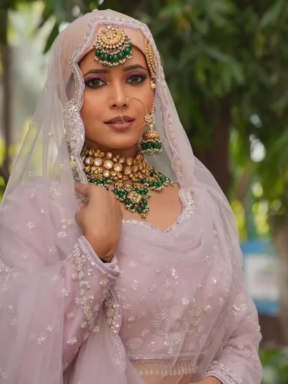 A beautiful Muslim bridal look with a pastel pink outfit and green jewelry. The makeup is soft and elegant.