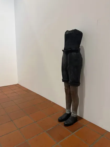 A striking sculpture standing in the corner of the gallery. Its placement in an otherwise empty corner draws attention to the form and texture of the piece, a lesson in the power of negative space.