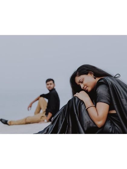 A minimalist and artistic pre-wedding shot of a couple in black, seated on a serene, empty landscape, conveying a sense of quiet intimacy.