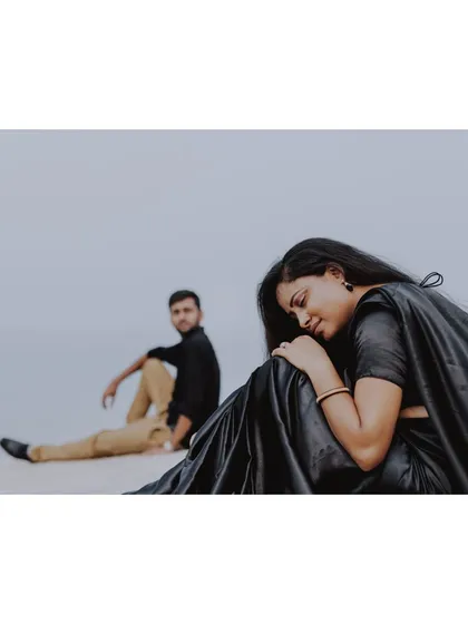 A minimalist and artistic pre-wedding shot of a couple in black, seated on a serene, empty landscape, conveying a sense of quiet intimacy.