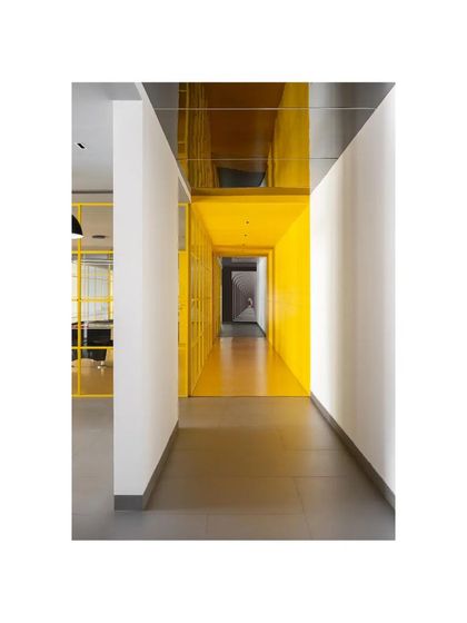 A view from a neutral-toned hallway into the vibrant yellow core of 'The Amber Encase' clubhouse. This contrast highlights the transition between different functional zones.