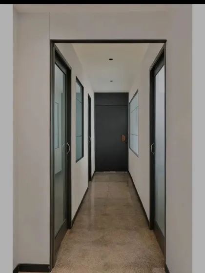 A view down the main corridor of Project Rooftop. The symmetrical design, with its black-framed glass doors and polished concrete floor, creates a strong sense of perspective and order. The solid black door at the end provides a clear focal point.