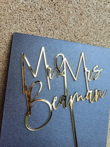 The "Mr & Mrs Beayman" topper against a textured background, highlighting its sharp lines and modern aesthetic.