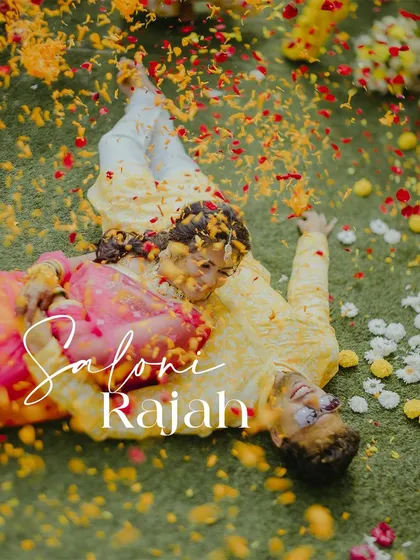 A unique aerial shot of the couple lying on the grass, covered in flower petals, capturing a moment of playful romance during their Haldi.