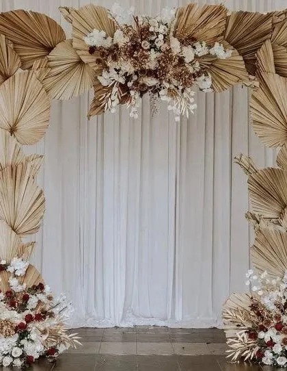 An elegant and simple boho backdrop idea. The arch is crafted entirely from dried palm leaves and accented with white and neutral florals, creating a beautiful, textured frame for a ceremony or photo corner.