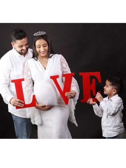 The family spells out "LOVE" with large red letters, with the 'O' perfectly framing the baby bump.