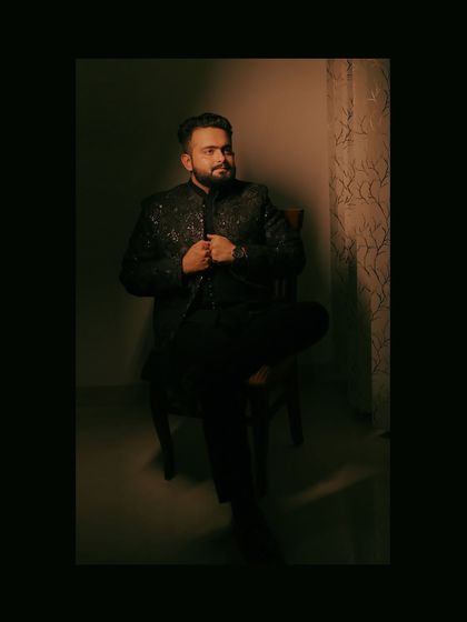 A moody, low-light portrait of the groom seated, his embroidered jacket catching the single light source.