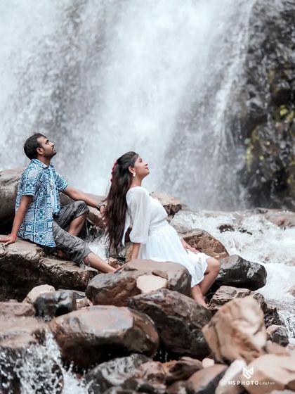 A peaceful moment with the couple sitting on rocks, looking up at the waterfall. This shot captures a sense of awe and tranquility.