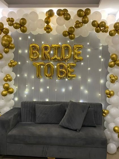 A classic and elegant 'Bride to Be' decoration for an at-home celebration. The white and gold balloon arch frames the seating area, while a curtain of fairy lights adds a warm, sparkling effect. (Also shown in images 5, 6).