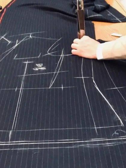 Precision in every cut. Our tailor uses traditional techniques to cut the fabric for a pinstripe suit, ensuring every pattern aligns perfectly for a seamless and professional finish.