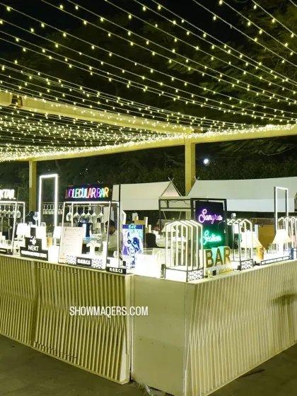 We design unique bar experiences for corporate events. This setup features multiple stations, including a molecular bar and cocktail bar, each with its own distinct neon signage and lighting under a canopy of fairy lights.