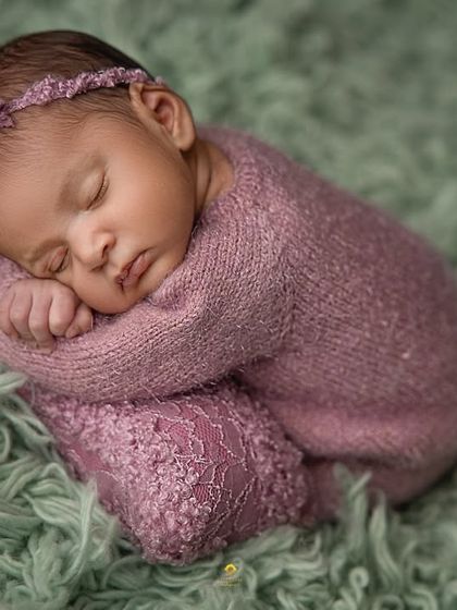 A classic newborn pose, with the baby curled up peacefully. The delicate lace details on the wrap and the matching headband add a touch of elegance to this simple portrait.