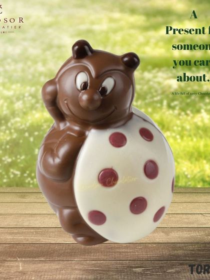 A whimsical chocolate tortoise figure holding a large, polka-dotted egg made of white chocolate.