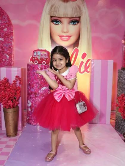The birthday girl strikes a pose at her Barbie-themed party. The all-pink backdrop with the iconic Barbie logo makes her feel like a star.
