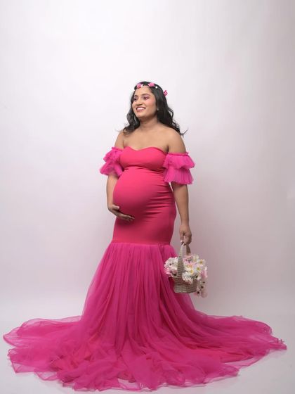 A full-length view of the popular hot pink mermaid gown. Accessorized with a flower crown and basket, this studio photo shows how you can personalize your maternity shoot style.