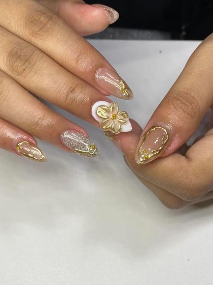 A close-up of a glamorous set featuring a nude base, glitter, and a stunning 3D gold flower with rhinestone accents.