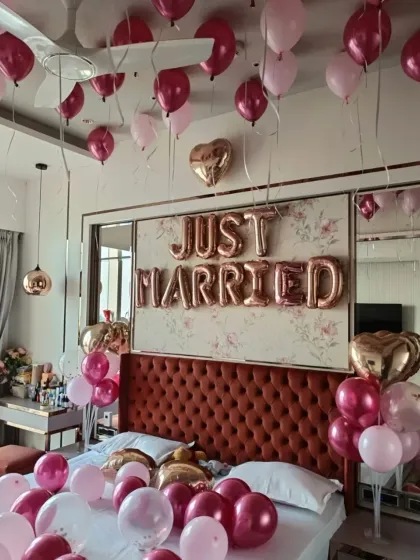 A beautiful 'Just Married' bedroom decoration. The room is filled with pink, magenta, and rose gold balloons on the ceiling and bed, with large foil letters above the headboard, creating a romantic and celebratory welcome for the newlyweds.