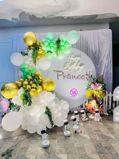 An elegant jungle-themed setup for a second birthday. This decoration features a white, green, and gold balloon arch, a personalized backdrop, a neon sign, and a light-up number '2'.