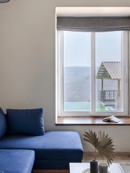 A cozy seating nook with a deep blue L-shaped sofa offers a comfortable spot to enjoy the view. The large window frames the surrounding landscape, making nature a part of the interior design.