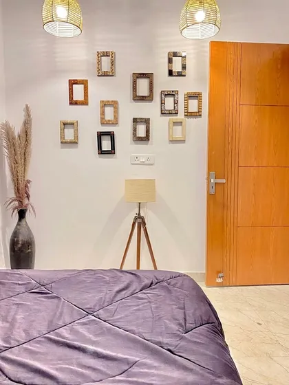 A view from the bed showing the minimalist decor, including a gallery wall of empty frames and a modern tripod lamp.