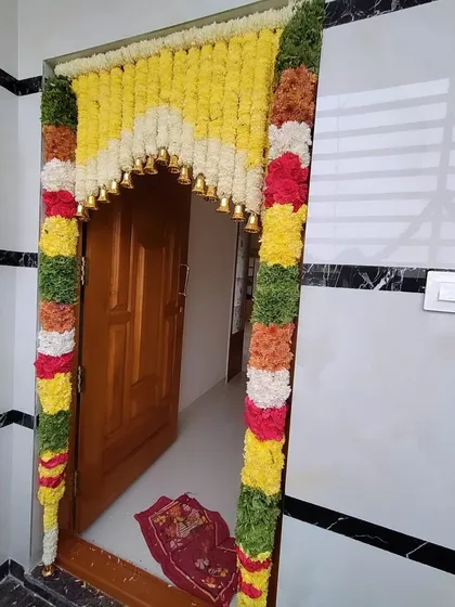 For home ceremonies, I create beautiful entrance decor using fresh flower garlands. This design features a dense floral arch with traditional bells for an auspicious touch.