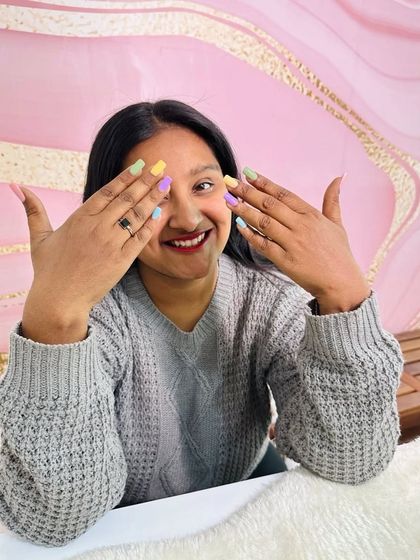 The cutest client showing off her first-ever set of nail extensions, a beautiful mix of pastel colors.