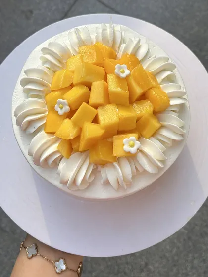 An overhead view of the Mango Dream Cake, showing the generous pile of fresh Safeda mangoes and delicate flower details.
