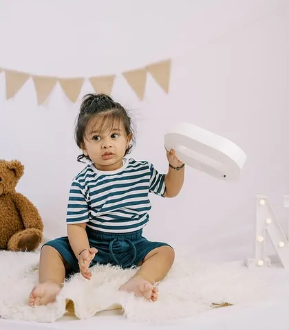 A candid moment from a first birthday shoot, with the little one playing with the light-up "ONE" letters.